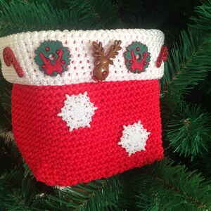 May include: Red crocheted Christmas stocking with white snowflakes and a white crocheted top with green and red embellishments.