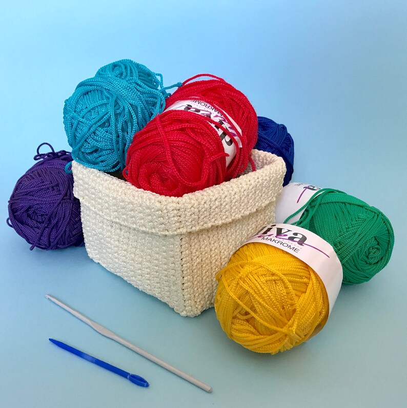 May include: A white crocheted basket filled with colorful yarn balls. The yarn is in shades of blue, red, yellow, purple, and green. The yarn is labeled "Diva Makrome".