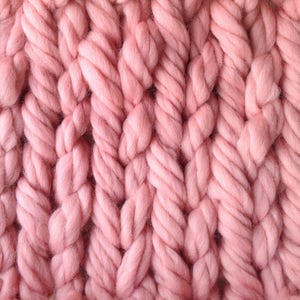 Op de afbeelding: Close-up van een roze gebreide stof met een dik kabelbreipatroon.