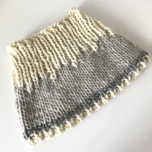 May include: A knitted cowl with a cream and gray color gradient. The cowl has a gray trim around the edge.