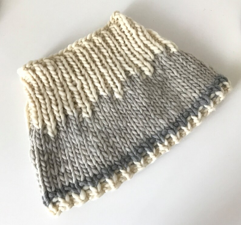 May include: A knitted cowl with a cream and gray color gradient. The cowl has a gray trim around the edge.