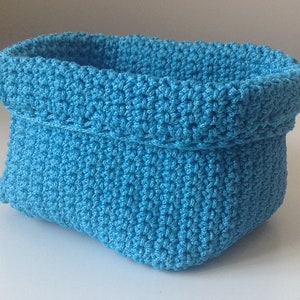 May include: A blue crocheted basket with a rounded shape. The basket is made with a textured stitch and has a folded top.