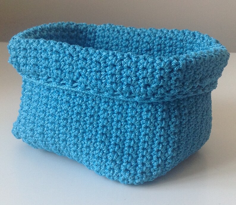 May include: A blue crocheted basket with a rounded shape. The basket is made with a textured stitch and has a folded top.
