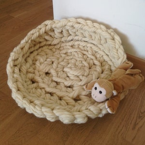 May include: A large, cream-colored, crocheted pet bed with a brown plush monkey toy inside.