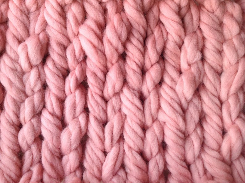 May include: Close-up of a pink knitted fabric with a chunky cable knit pattern.