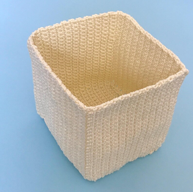 May include: A white crocheted square basket with a textured surface.
