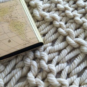May include: A closed book with a world map cover on a white crocheted blanket.