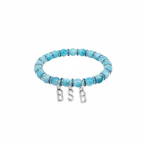 Könnte beinhalten: Ein hellblaues Perlenarmband mit silbernen Akzenten und drei baumelnden silbernen Anhängern mit der Aufschrift "BSB". Das Armband hat runde, hellblaue Perlen und kleinere, dekorative Perlen mit blauen Akzenten.