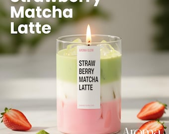 May include: Aroma Glow candle in a clear glass, layered with pink, white, and green wax, resembling a Strawberry Matcha Latte. The candle has a lit wick and a label that reads "Strawberry Matcha Latte." Fresh strawberries and matcha powder are also visible.