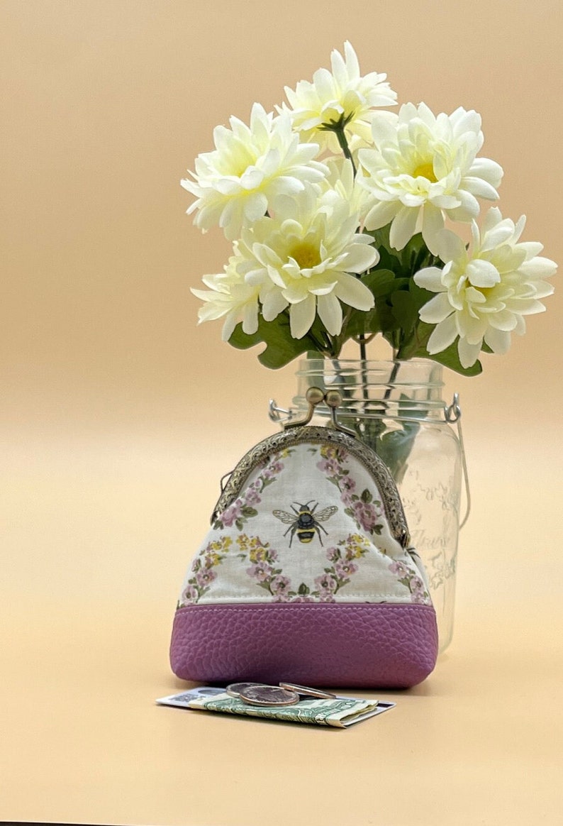 Coin purse clasp bee. Off white background with black bee yellow stripes. Purple & yellow flowers with green leaves. Purple faux leather on bottom. Bronze kiss clasp.