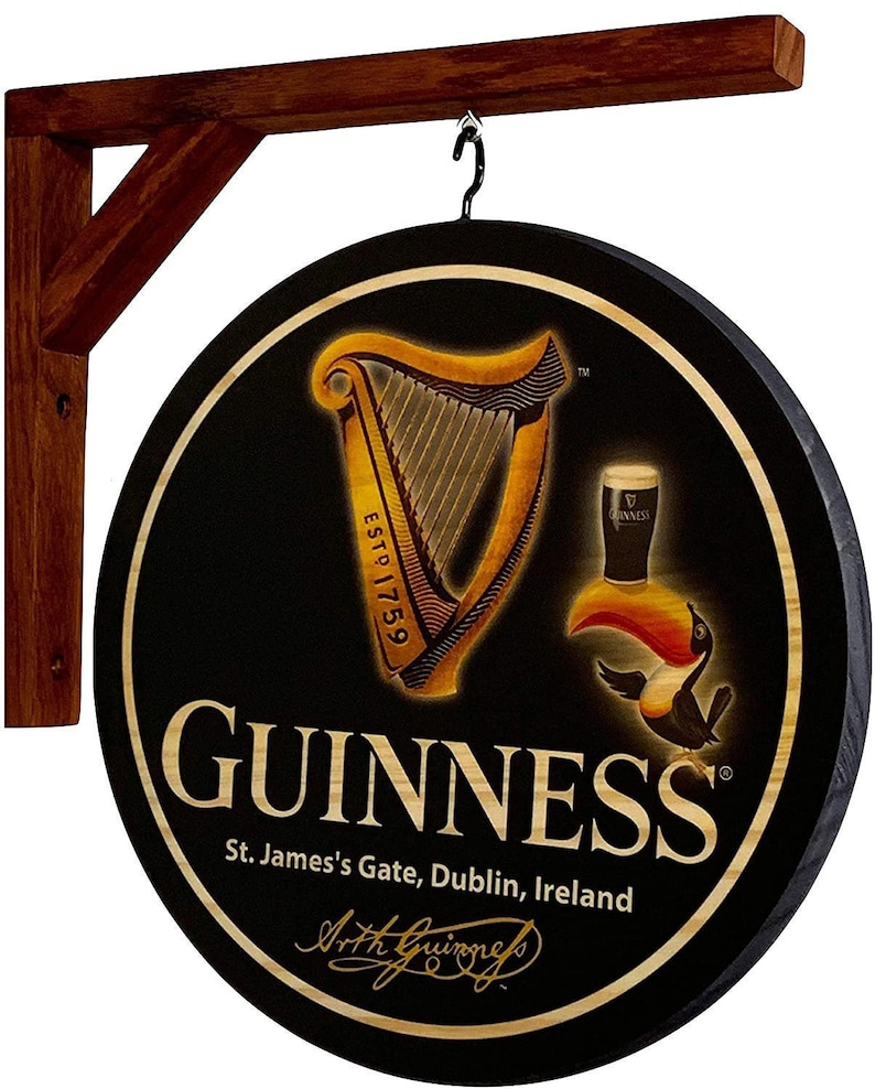 May include: A round, black wooden sign with a gold Guinness harp logo, the text "ESTD 1759", and the words "GUINNESS St. James's Gate, Dublin, Ireland" in white. The sign has a wooden frame and a metal hook for hanging.