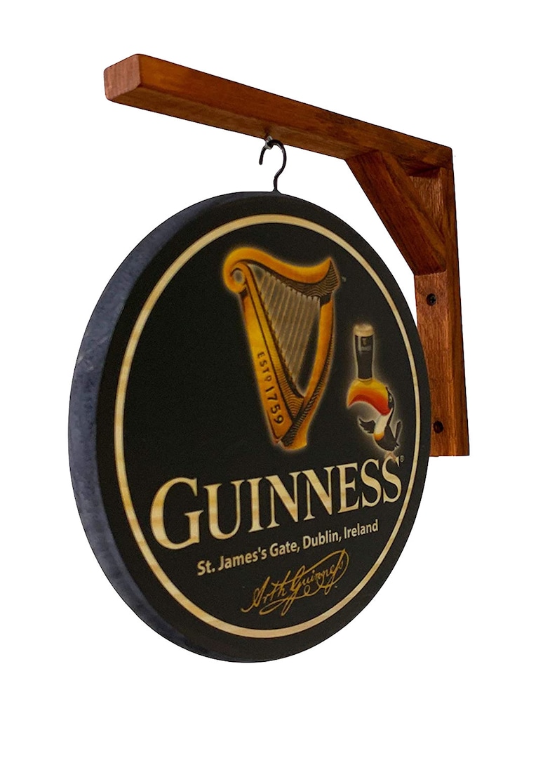 May include: A round wooden sign with a black background and a gold Guinness harp logo. The sign also features the text "GUINNESS", "St. James's Gate, Dublin, Ireland", and a signature. The sign is hanging from a wooden bracket.