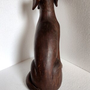 May include: A dark brown wooden dog figurine sitting with its tail curled. The figurine is carved with details and has a distressed finish.