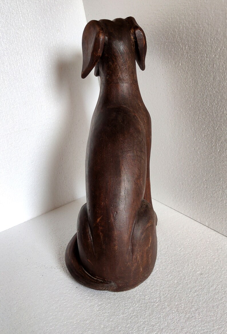 May include: A dark brown wooden dog figurine sitting with its tail curled. The figurine is carved with details and has a distressed finish.