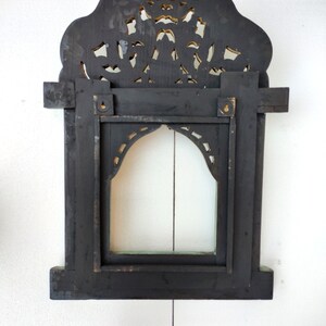 May include: Black wooden frame with intricate carved details and a gold-painted finish. The frame has a rectangular opening with a smaller arched opening inside. The frame is designed to hold a mirror or picture.