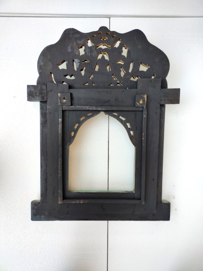 May include: Black wooden frame with intricate carved details and a gold-painted finish. The frame has a rectangular opening with a smaller arched opening inside. The frame is designed to hold a mirror or picture.