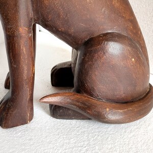 May include: A dark brown wooden sculpture of a dog sitting with its tail curled around its legs.