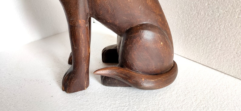 May include: A dark brown wooden sculpture of a dog sitting with its tail curled around its legs.