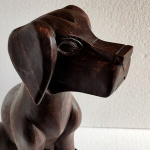 May include: A dark brown wooden sculpture of a dog sitting with its head tilted to the side. The dog has a long snout and large ears.