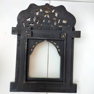 May include: A black wooden frame with intricate gold carvings. The frame has a rectangular opening with a clear glass pane. The frame is designed to hang on a wall.