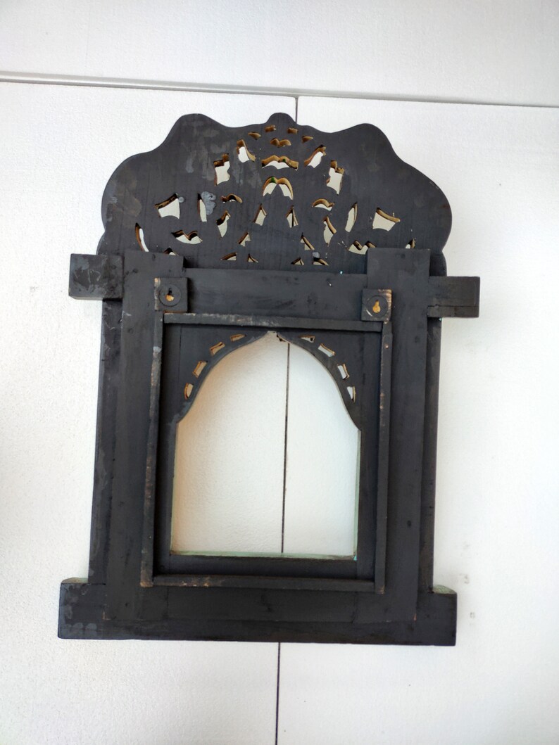 May include: A black wooden frame with intricate gold carvings. The frame has a rectangular opening with a clear glass pane. The frame is designed to hang on a wall.