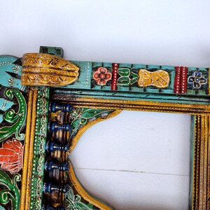 May include: A teal blue wooden frame with intricate carvings and colorful paint details. The frame features an elephant design, floral motifs, and geometric patterns. The frame is perfect for adding a touch of Indian style to your home decor.