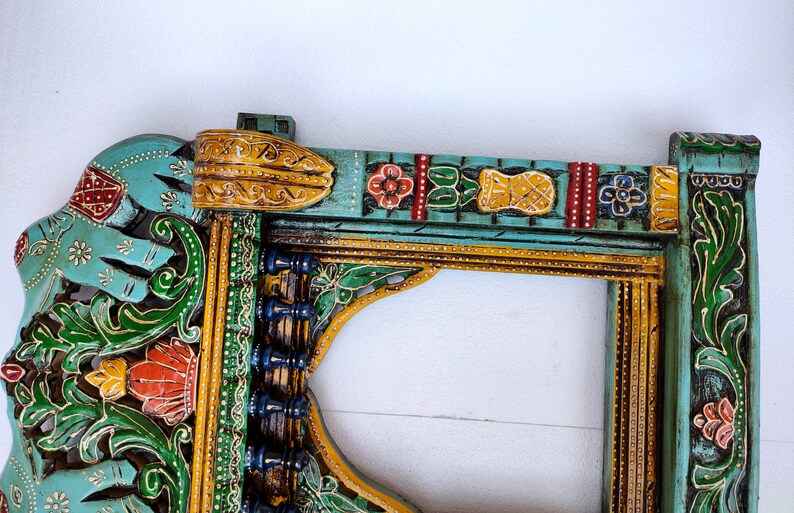 May include: A teal blue wooden frame with intricate carvings and colorful paint details. The frame features an elephant design, floral motifs, and geometric patterns. The frame is perfect for adding a touch of Indian style to your home decor.