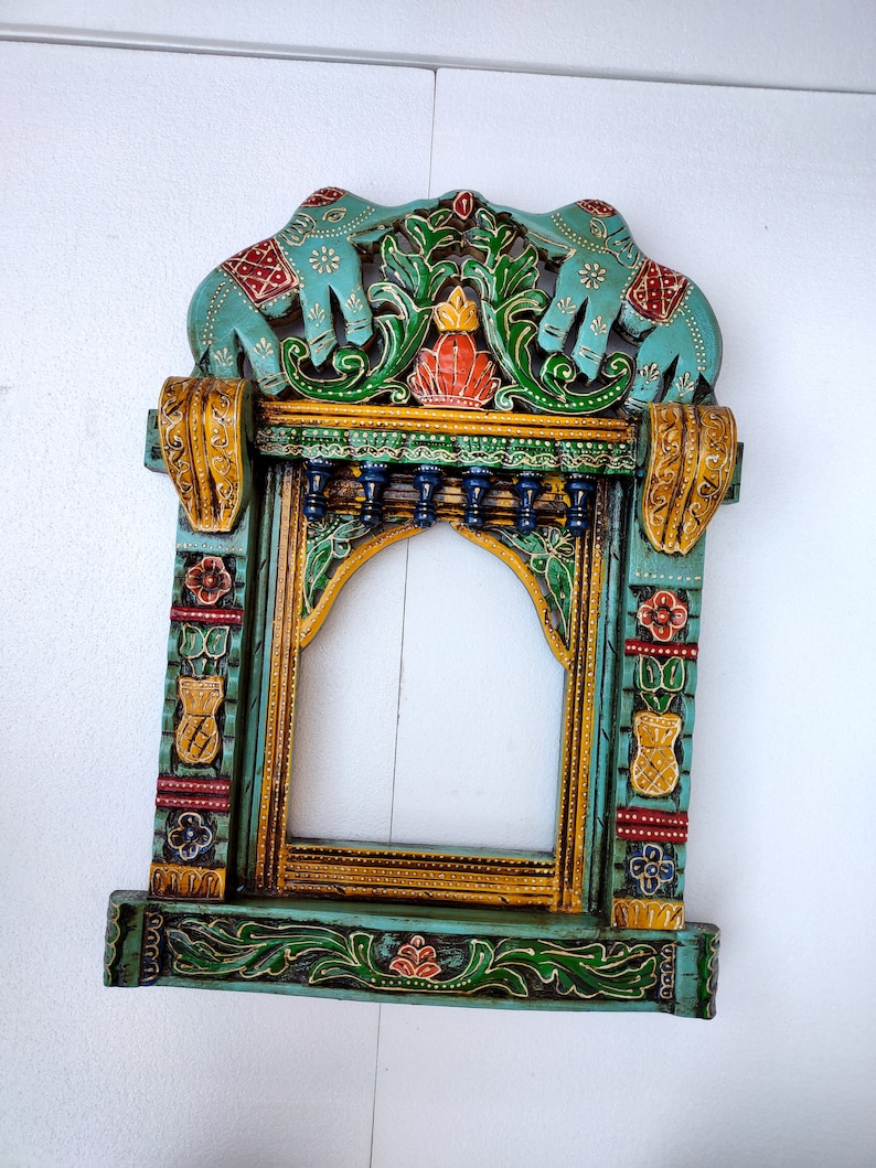 May include: A teal blue wooden frame with intricate carvings of elephants, flowers, and leaves. The frame is painted in gold, red, and green colors.