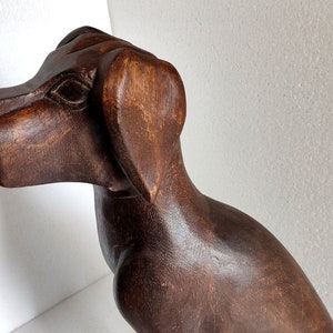 May include: A dark brown wooden sculpture of a dog. The dog is sitting with its head turned to the side and its ears perked up.