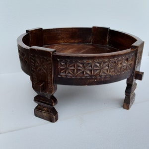 May include: A round wooden table with intricate carvings around the top and legs. The table is dark brown and has a rustic look.