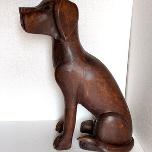 May include: A dark brown wooden sculpture of a dog sitting with its head turned to the side. The dog has a long snout and floppy ears.