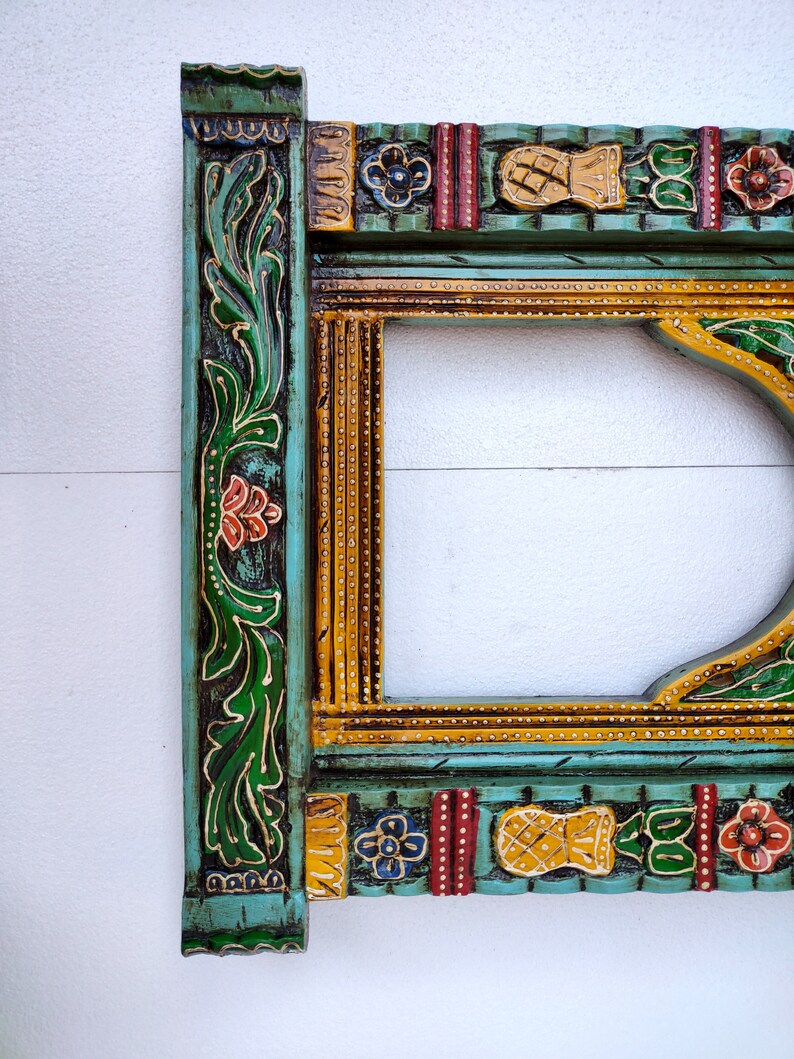 May include: A decorative wooden frame with intricate carvings and colorful paint. The frame is painted in shades of green, yellow, red, and blue. The frame has a floral design and a geometric pattern.