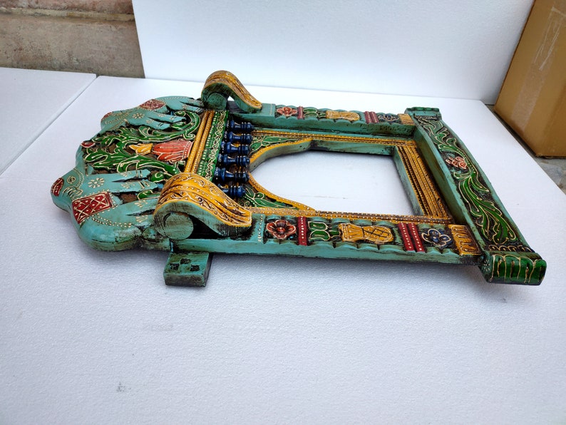 May include: A teal blue wooden frame with intricate carvings and colorful paint details. The frame features a carved archway design with floral and elephant motifs.