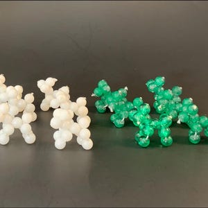 May include: Four white and four green beaded dog figurines are arranged on a dark surface. The dogs are made of small, round beads strung together to form the shape of a dog. The white dogs are on the left, and the green dogs are on the right.