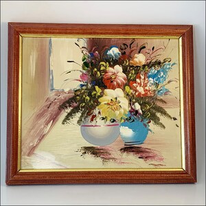 May include: A framed painting of a still life featuring a bouquet of colorful flowers in two ceramic vases. The flowers are in shades of pink, yellow, blue, and white. The vases are a light blue and a white with a pink stripe.