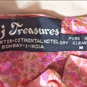 May include: A black label with white text that reads "Taj Treasures", "TAJ INTER-COTINENTAL HOTEL", "BOMBAY-1-INDIA", "PURE SILK", "DRY CLEAN ONLY", and "M".