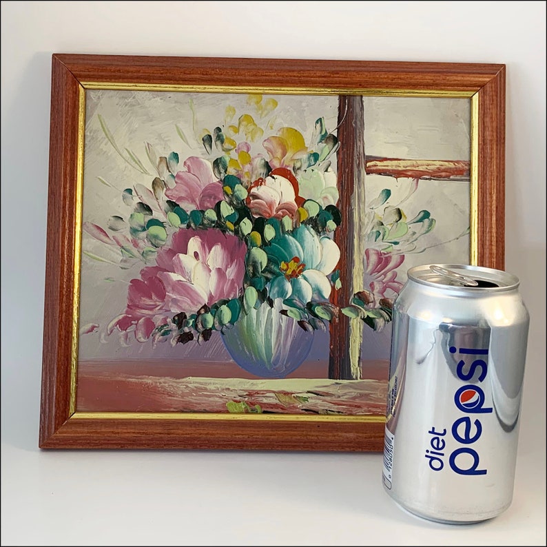 May include: A framed painting of a colorful floral arrangement in a blue vase. The painting is set against a light background and features a wooden frame.