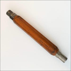 May include: An antique tool with a wooden handle and metal ends. The handle is a warm orange color, with the text "WARREN CORPORATION" and "BRACER DIVISION" printed on it. The metal ends are a silver color.