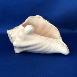 May include: A pink ceramic seashell planter with a white pearl inside. The seashell has a textured surface and is a decorative item.