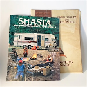May include: A 1980 Shasta travel trailer and fifth wheel brochure and owner's manual. The brochure cover features a white travel trailer parked in a wooded area with a family sitting in folding chairs around a campfire, with text reading SHASTA.