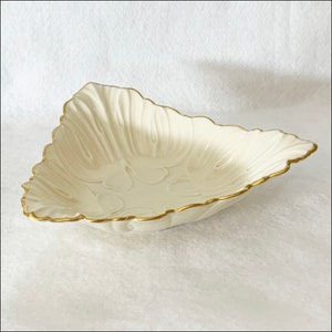May include: A white triangular serving dish with a gold rim and a floral design. The dish is made of fine china and is perfect for serving snacks or desserts.