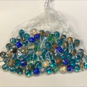 May include: A clear plastic bag filled with a collection of small, round glass marbles. The marbles feature a variety of translucent colors, including shades of blue, green, and clear, with some containing internal swirls and iridescent finishes.