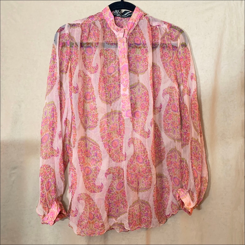 May include: A pink sheer blouse with a paisley print. The blouse has a button-up front and long sleeves.
