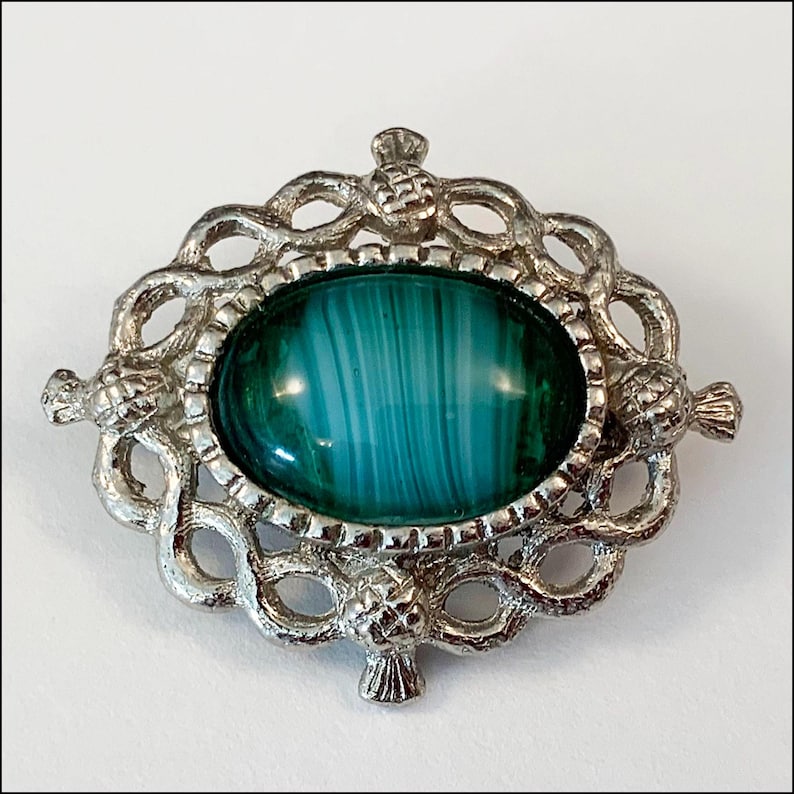 May include: A silver brooch with a green and white agate stone set in a Celtic knot design. The brooch is decorated with four thistle motifs.