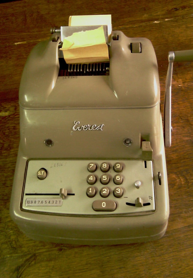 Puede incluir: Una m&aacute;quina de sumar vintage de color gris con un soporte para rollo de papel, una palanca y un teclado num&eacute;rico con teclas del 0 al 9. La m&aacute;quina tiene la palabra "Everest" impresa en la parte delantera.
