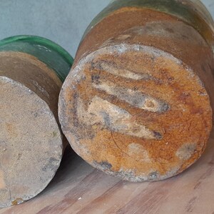 May include: Two cylindrical wooden objects with a weathered, rustic appearance. The smaller one has a green glass top, while the larger one is a darker brown with visible wood grain and a rusty texture. The objects are on a wooden surface.