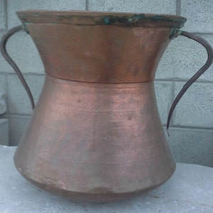 May include: A large copper pot with two iron handles. The pot has a wide mouth and a rounded bottom. The copper has a hammered finish and is slightly tarnished.