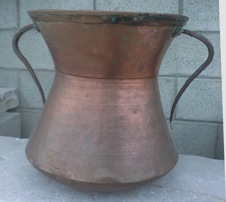 Puede incluir: Una olla grande de cobre con dos asas de hierro. La olla tiene una boca ancha y un fondo redondeado. El cobre tiene un acabado martillado y est&aacute; ligeramente deslustrado.