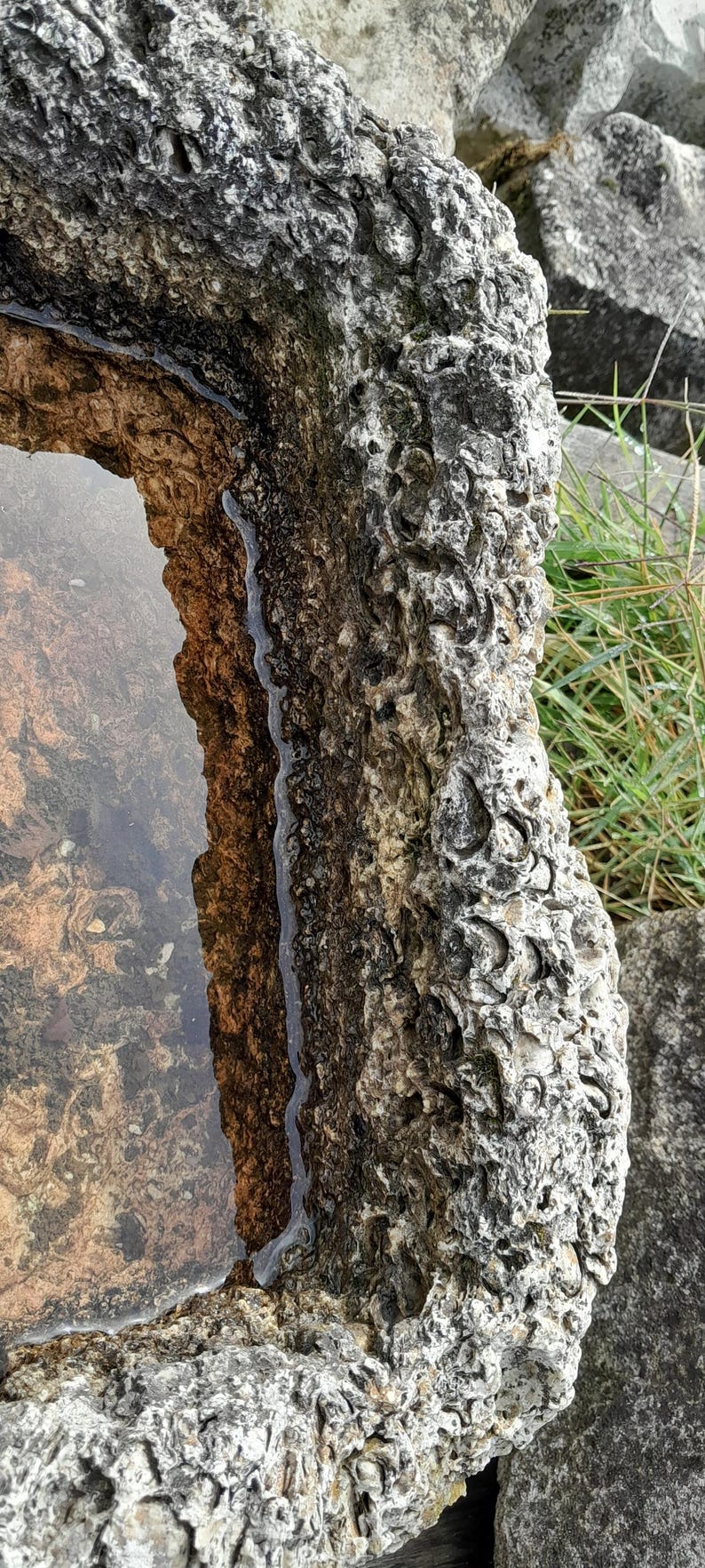 May include: A close-up of a stone birdbath with a rough, textured surface. The birdbath is filled with water and has a natural, rustic look.
