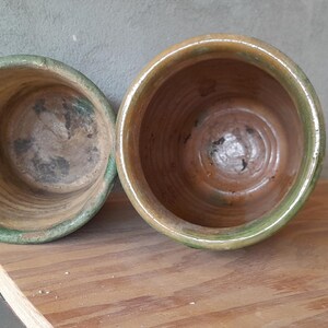 May include: Two empty, weathered ceramic pots with a green rim and a brown interior. The pots are sitting on a wooden surface. The pots are likely for plants.